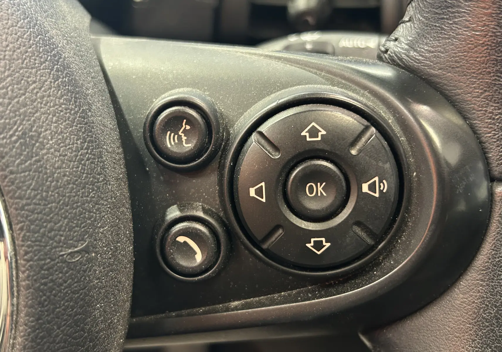 Gros plan sur les commandes multifonctions noires du volant côté gauche d’une MINI 5 portes bleu 2015.