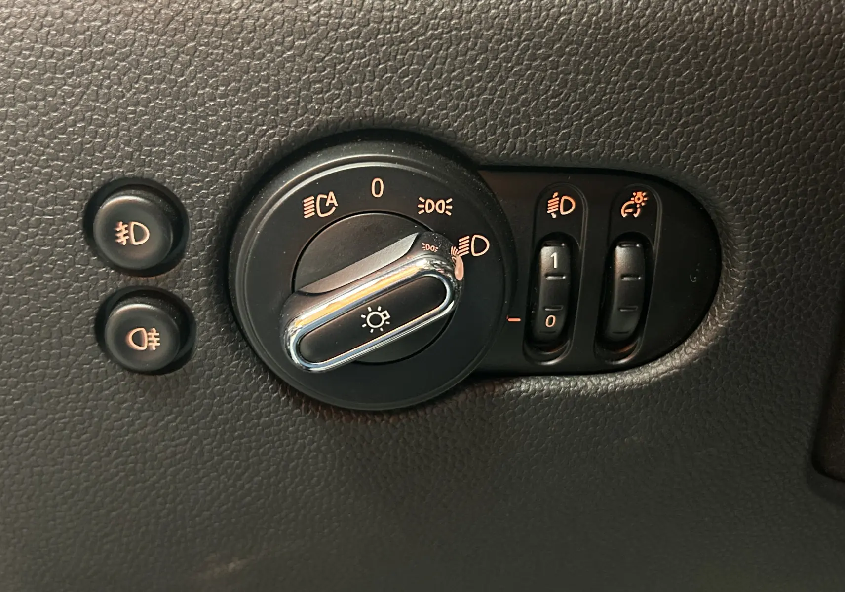Gros plan sur la commande d’éclairage et réglages des phares du tableau de bord d’une MINI 5 portes bleu.