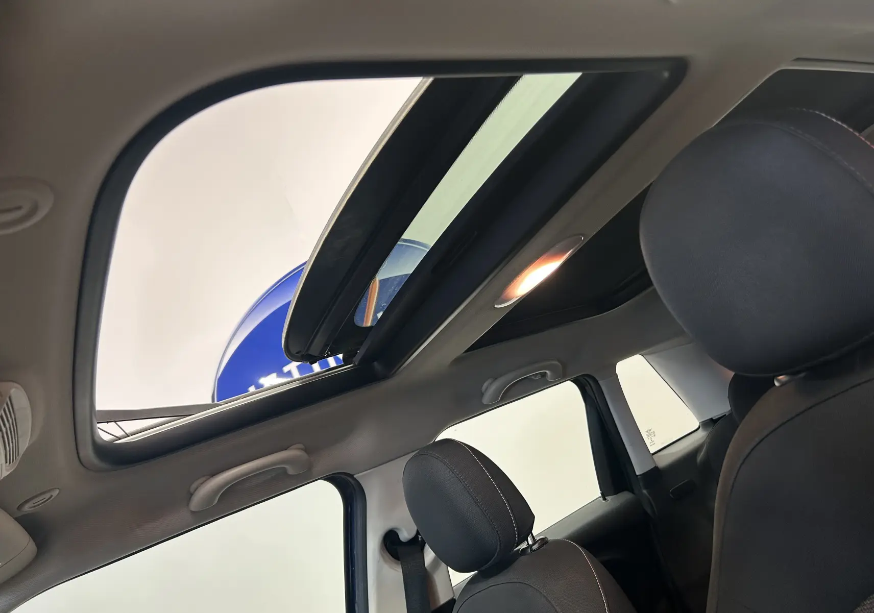 Vue intérieure du toit ouvrant panoramique de la MINI 5 portes Cooper D bleu, avec sièges avant en tissu noir.