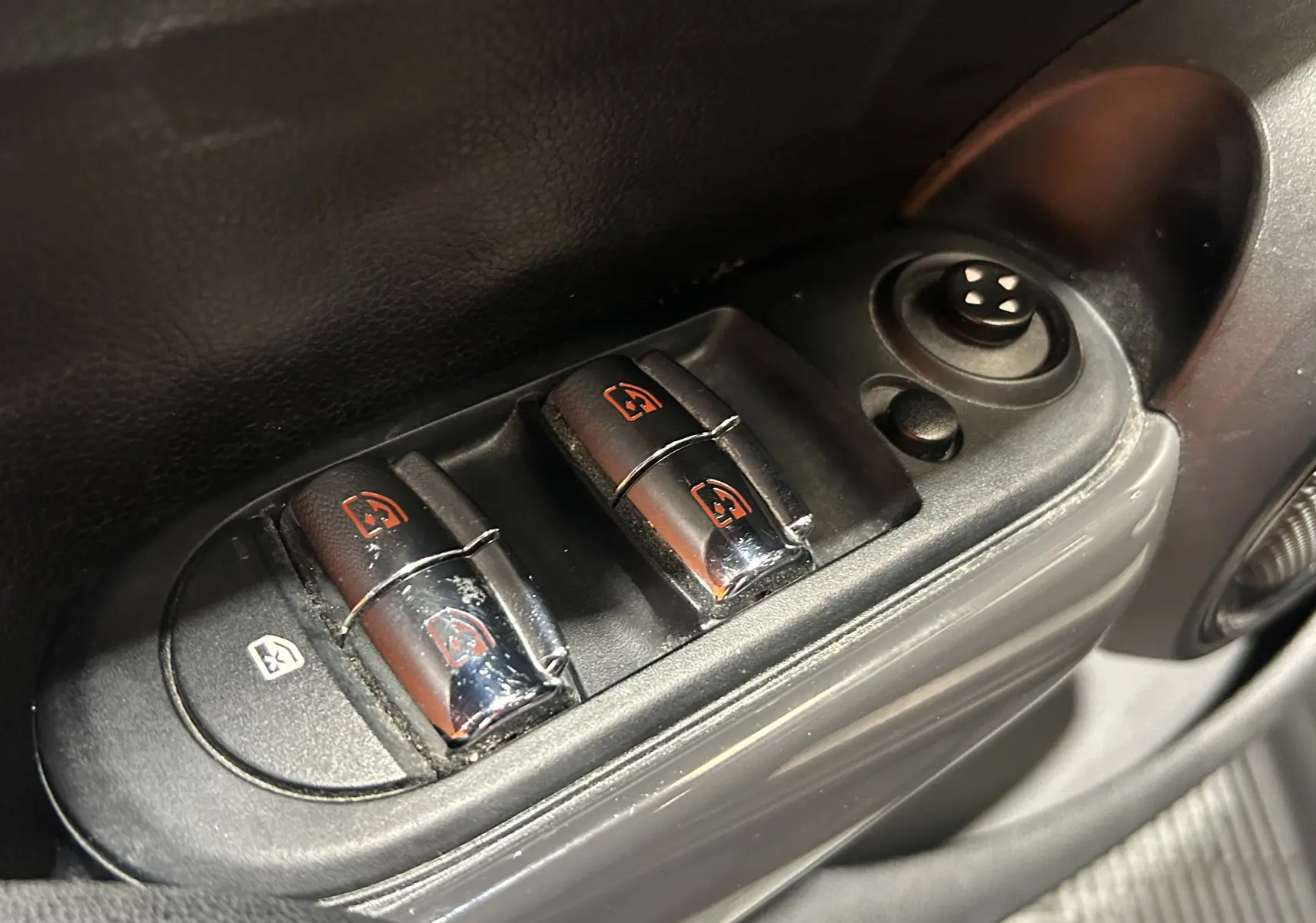 Gros plan sur les commandes des vitres électriques côté conducteur d’une MINI 5 portes bleu, avec réglage des rétroviseurs.