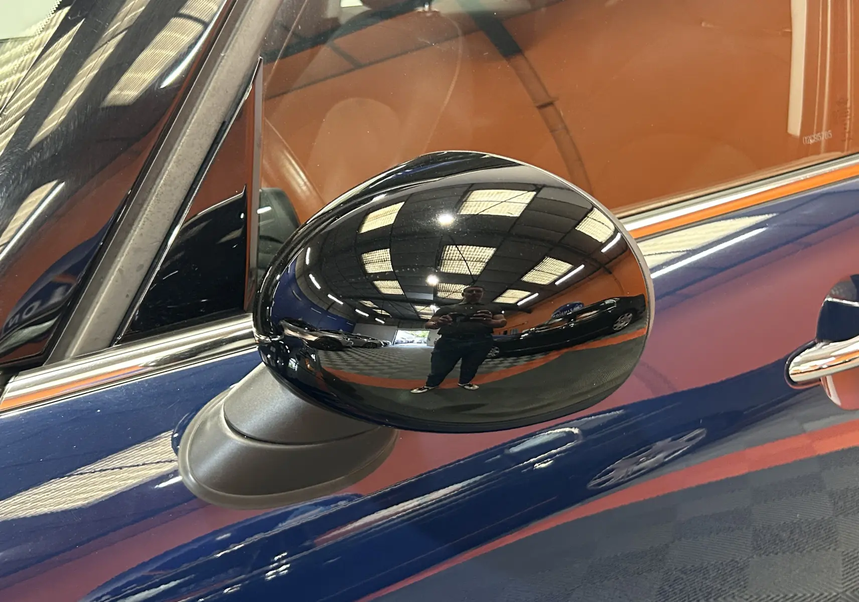 Rétroviseur noir en gros plan côté gauche d'une MINI 5 portes bleu avec intérieur cuir marron visible.