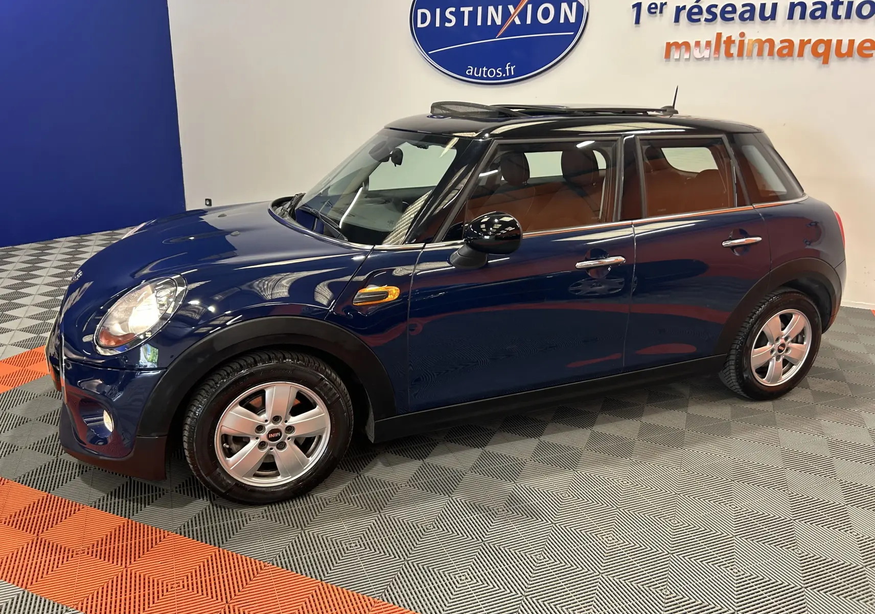 Vue côté gauche en 3/4 avant d'une MINI 5 portes Cooper D bleu avec toit ouvrant et intérieur cuir marron.