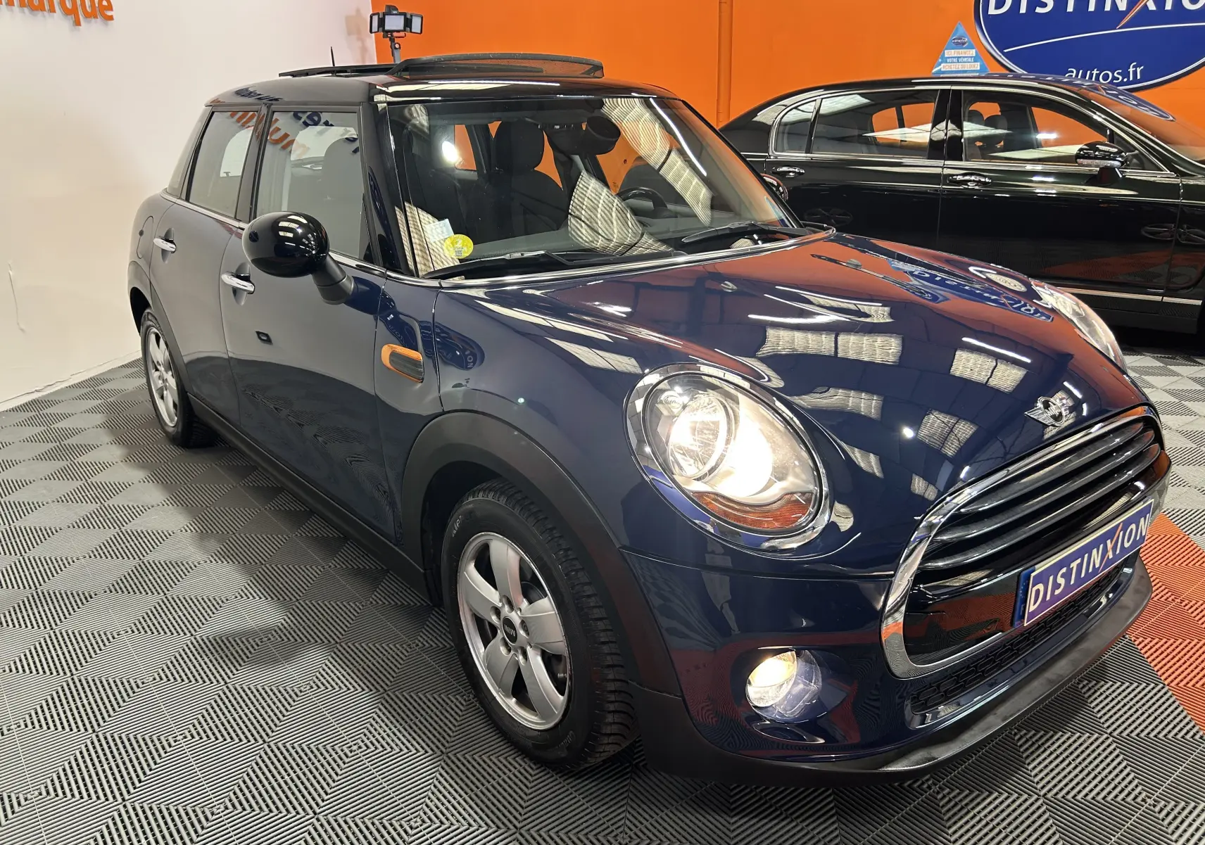 Vue 3/4 avant droite d'une MINI 5 portes Cooper D bleu foncé avec toit ouvrant dans un showroom.