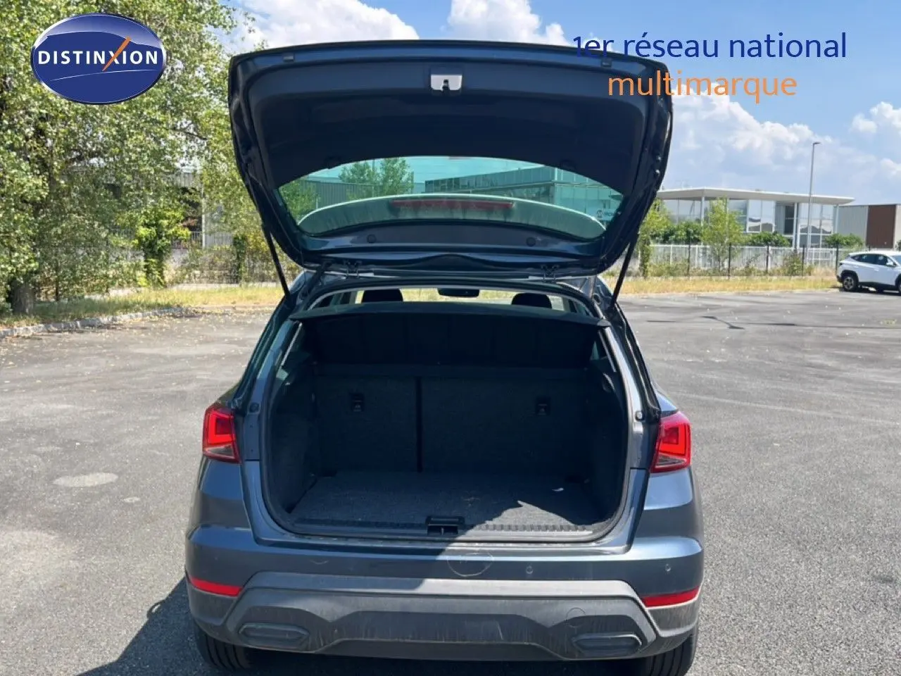 Vue arrière d'un SEAT Arona gris Magnetic avec coffre ouvert, toit blanc visible sous un ciel ensoleillé.