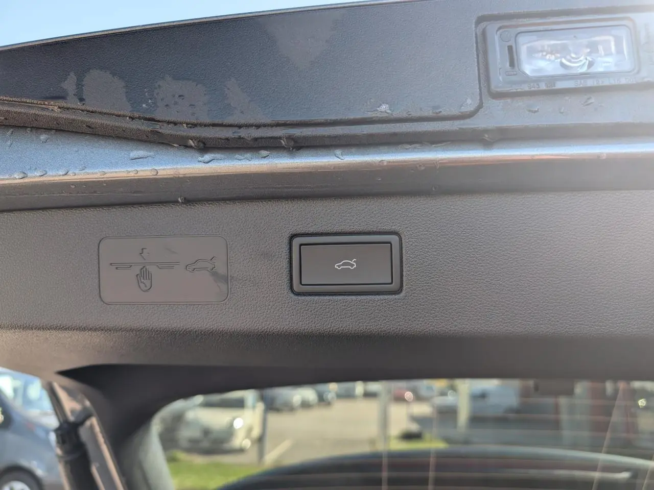 Bouton d'ouverture électrique du coffre sur le hayon intérieur d'un Volkswagen T-Roc gris, vue rapprochée.