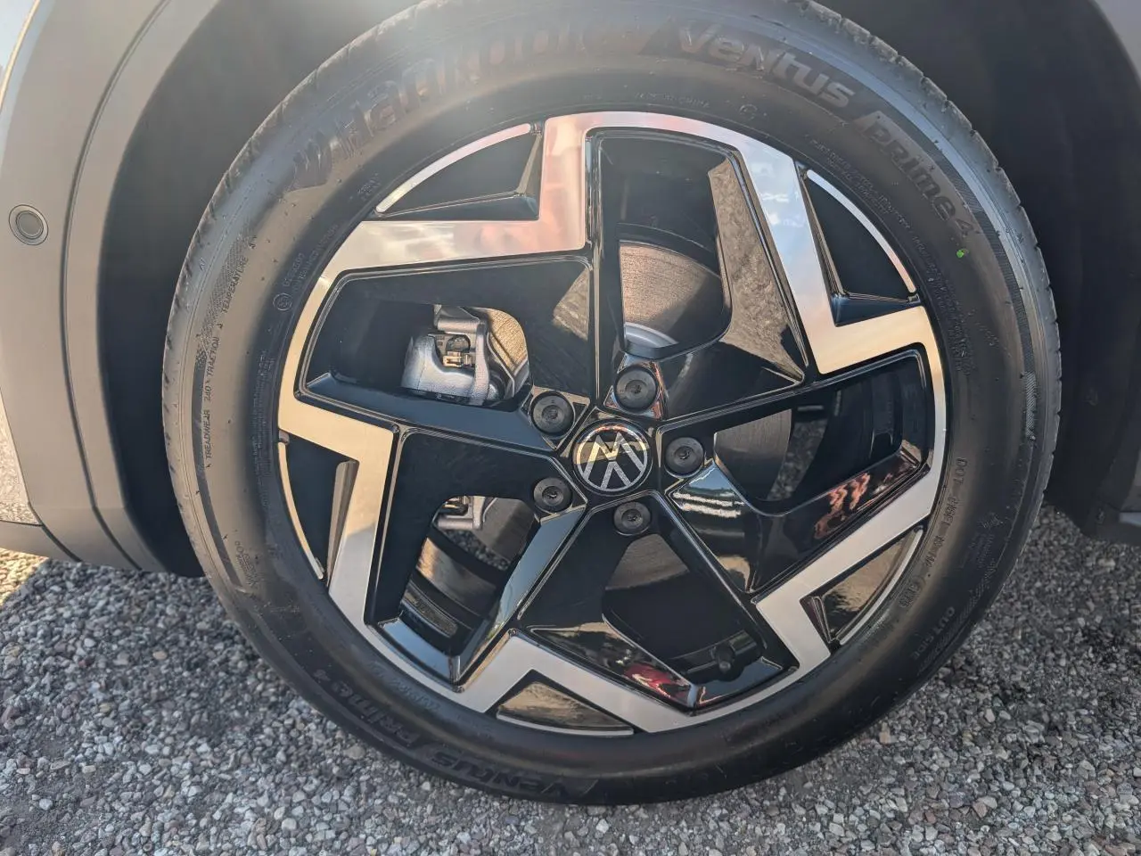 Gros plan sur la jante 18 pouces bicolore noire et argentée du Volkswagen T-Roc gris, avec logo VW au centre.