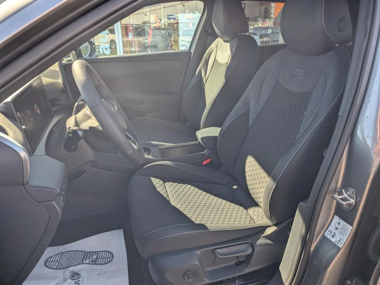 Vue intérieure côté gauche du poste de conduite du Volkswagen T-Roc gris, avec sièges sport R-Line en tissu et volant multifonction cuir.