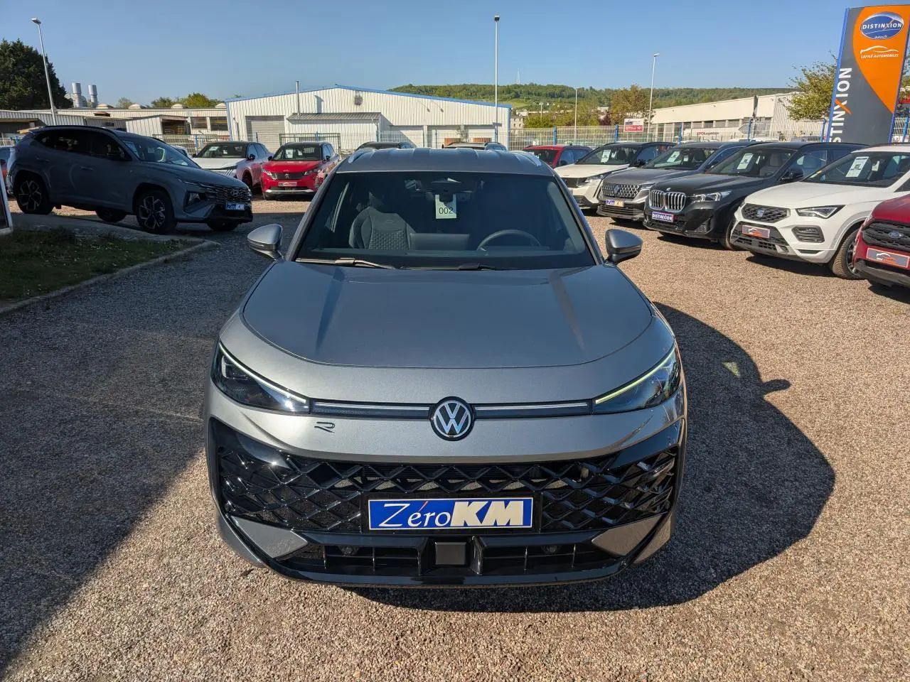 Volkswagen T-Roc gris métallisé en vue frontale, avec calandre noire et logo VW éclairé.