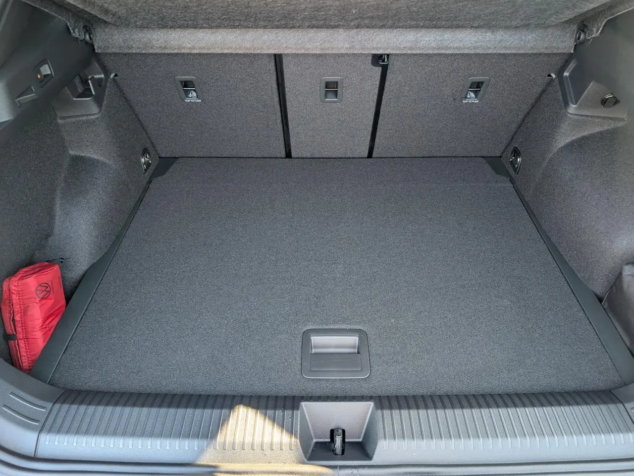 Vue plongeante sur le coffre gris du Volkswagen T-Roc 1.5 eTSI Hybrid Evo2 avec tapis plat et trousse de secours rouge.