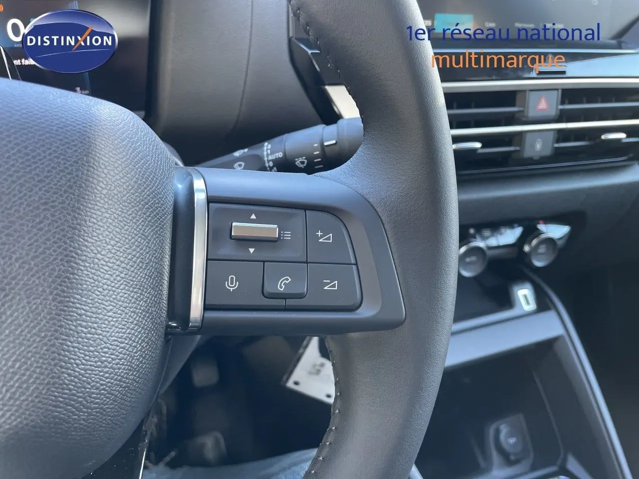 Gros plan sur les commandes gauche du volant d’une Citroën C4 hybride 2026, avec tableau de bord et console en arrière-plan.