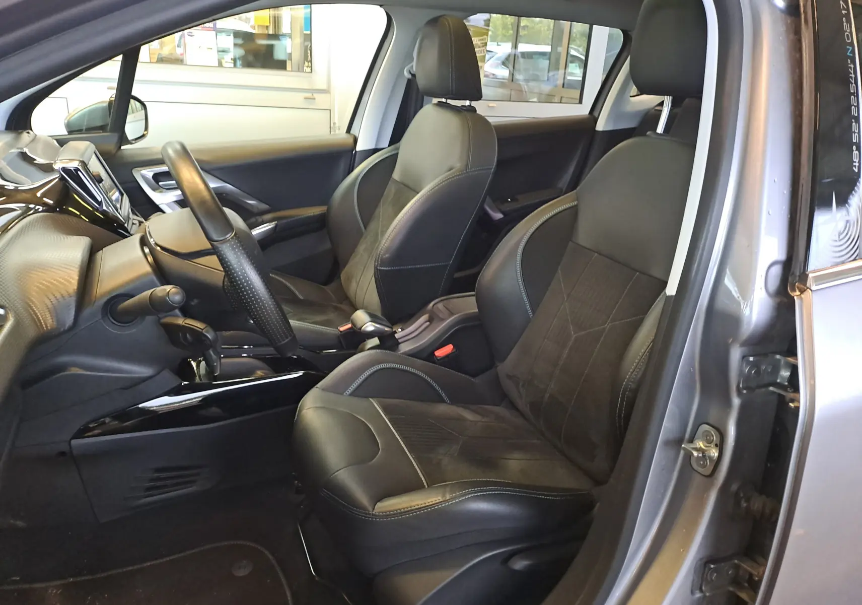Intérieur vue côté conducteur du Peugeot 2008 gris 2019, sièges noirs en cuir et alcantara avec console centrale brillante.