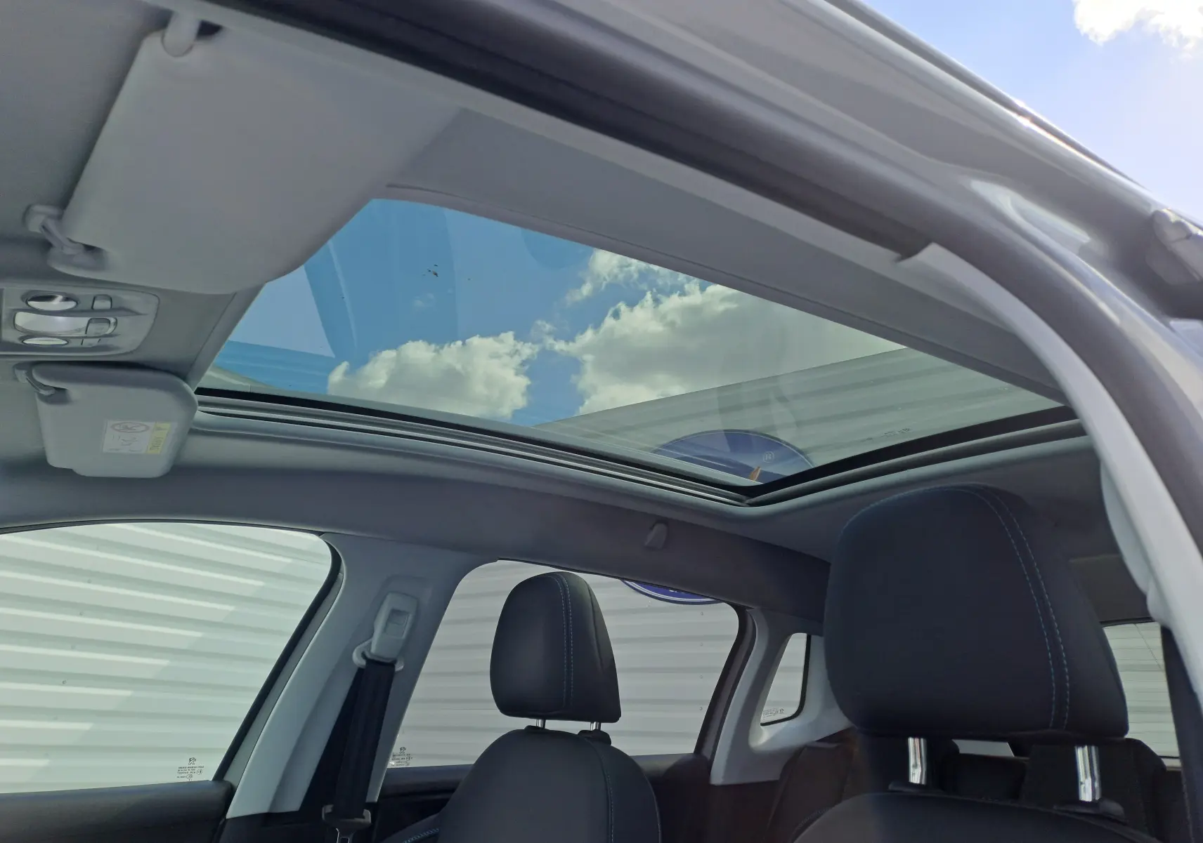 Vue intérieure du toit ouvrant panoramique et des sièges noirs du Peugeot 2008 gris 2019, côté gauche ouvert.