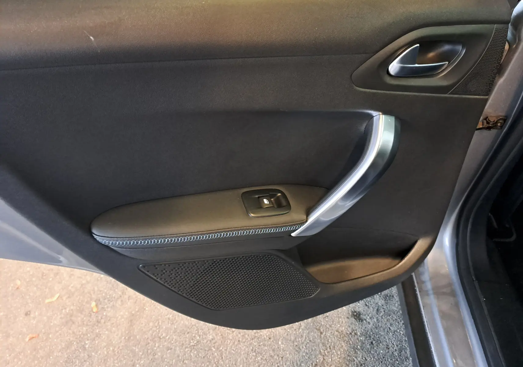 Gros plan sur la porte côté gauche d'une Peugeot 2008 gris 2019, avec poignée argentée et bouton de vitre électrique.