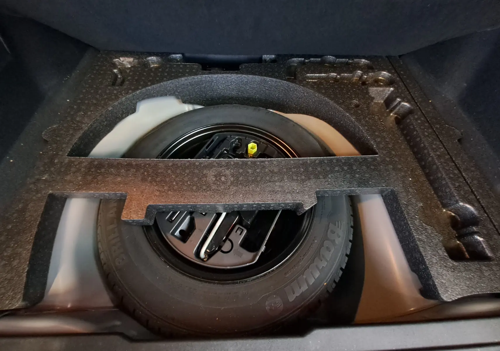 Roue de secours noire dans le coffre d'un Peugeot 2008 gris, avec outils de changement rangés dessus.