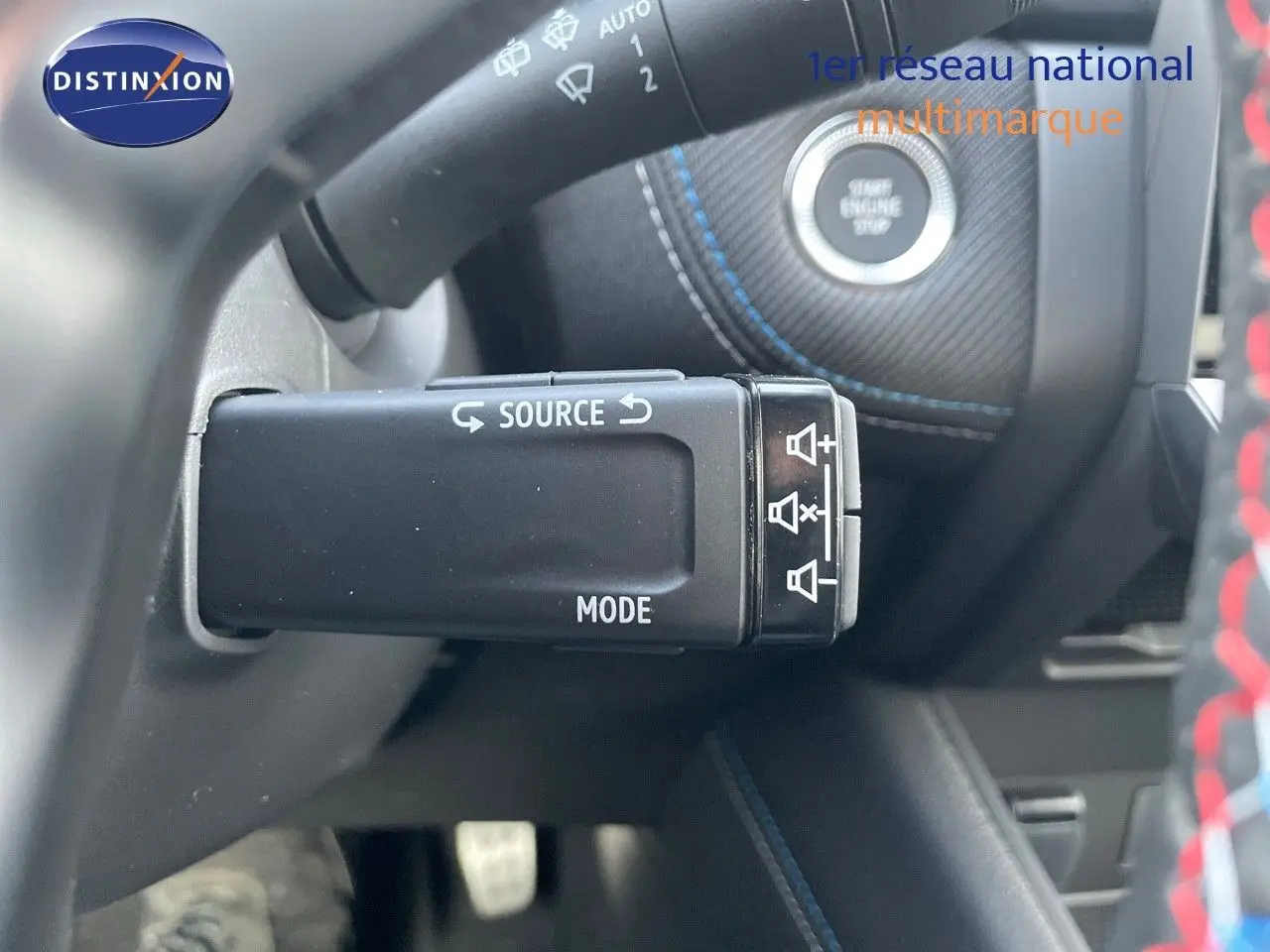 Gros plan sur la commande audio au volant et bouton start/stop avec surpiqûres bleues dans l'habitacle gris du Renault Symbioz.