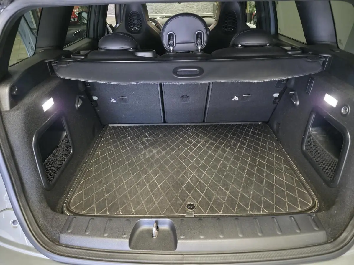 Coffre ouvert vu de l'arrière d'une MINI Clubman gris Moonwalk avec tapis de sol matelassé et banquette rabattable.