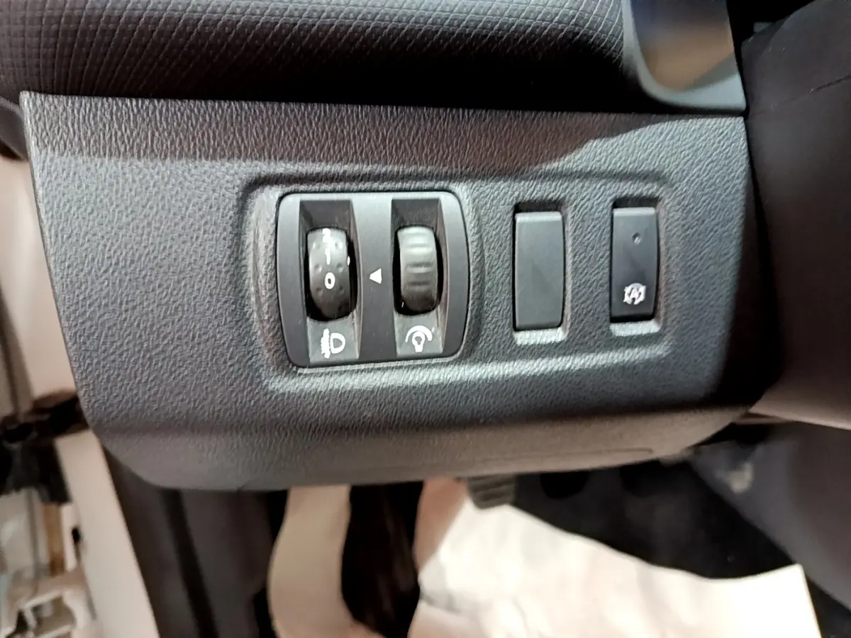 Gros plan sur les commandes de réglage des phares et du tableau de bord d’une Renault Clio Zen Energy dCi 75 blanche de 2016.