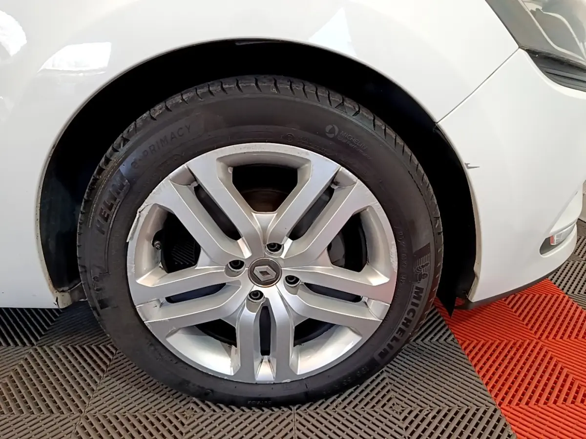 Gros plan sur la roue avant gauche d'une Renault Clio blanche, jante alliage argent avec logo Renault au centre.