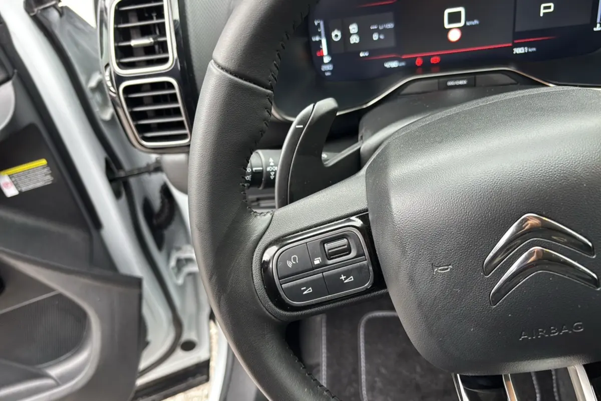 Gros plan sur le volant cuir multifonctions de la Citroën C5 Aircross Hybrid blanche, avec tableau de bord digital en arrière-plan.