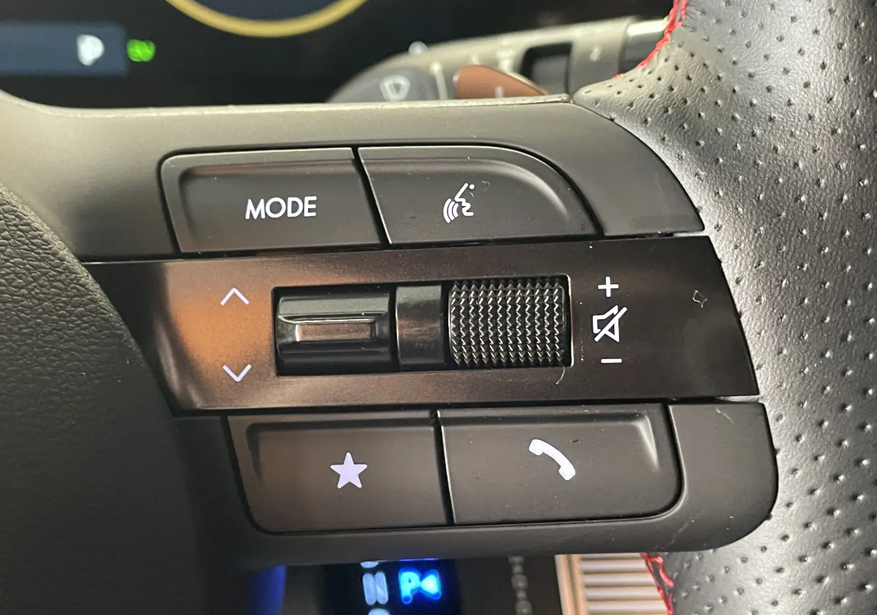 Gros plan sur les commandes du volant perforé avec surpiqûres rouges du Hyundai Tucson gris Ecotronic 2025.