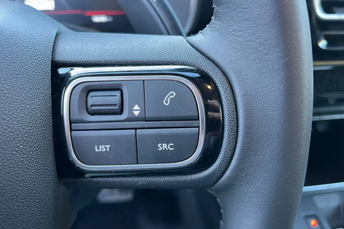 Gros plan sur les commandes gauche du volant cuir du Citroën C5 Aircross blanc okénite, version hybride 2025.