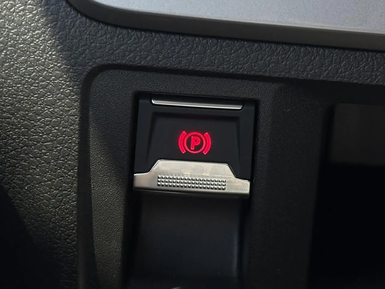 Gros plan sur le bouton de frein de stationnement électrique rouge dans l'habitacle noir du Citroën Jumpy.