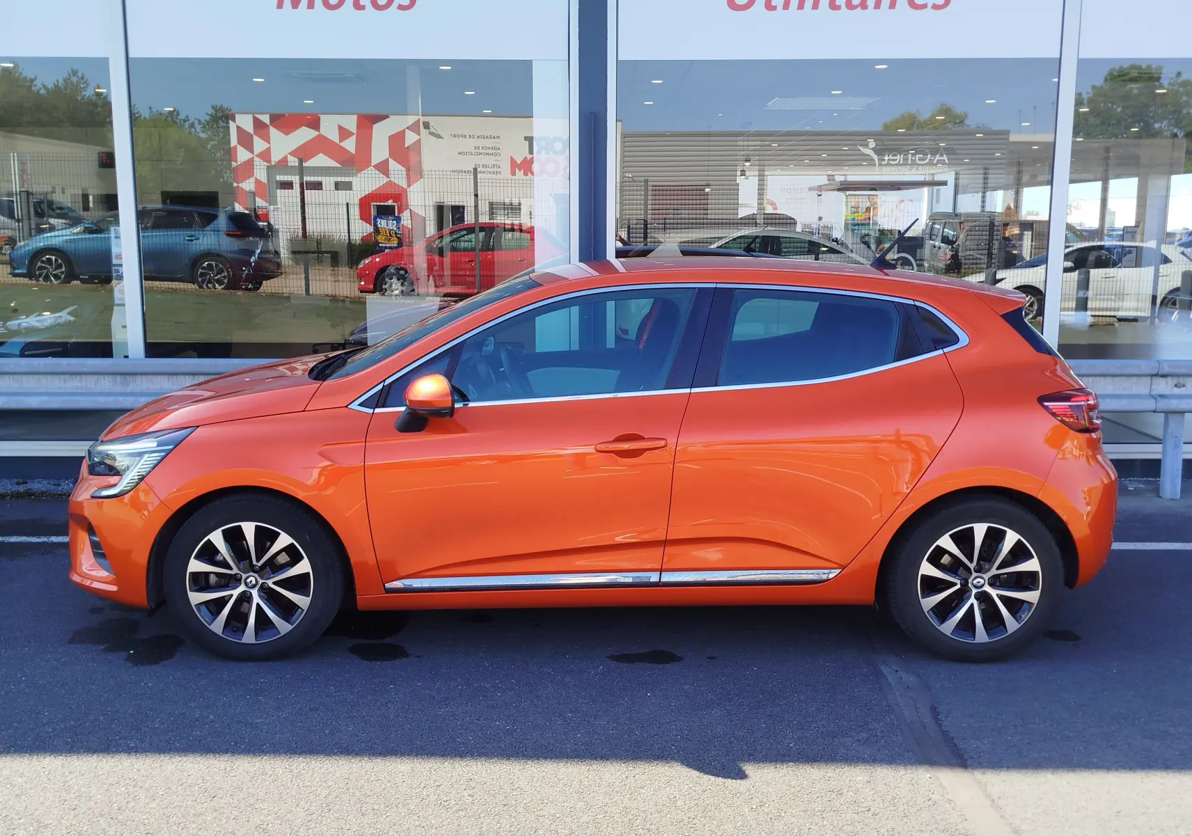 Profil côté gauche de la Renault Clio 1.6 E-Tech hybride 140ch Intens 2022 en Orange Valencia, avec jantes alliage et vitres teintées.