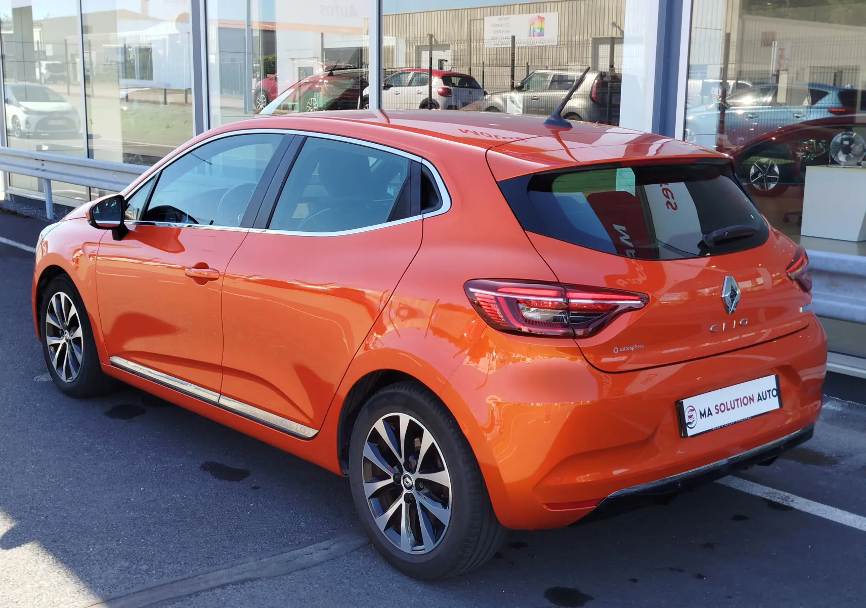 Renault Clio 1.6 E-Tech hybride orange Valencia vue 3/4 arrière droit, avec jantes alliage et vitres teintées.