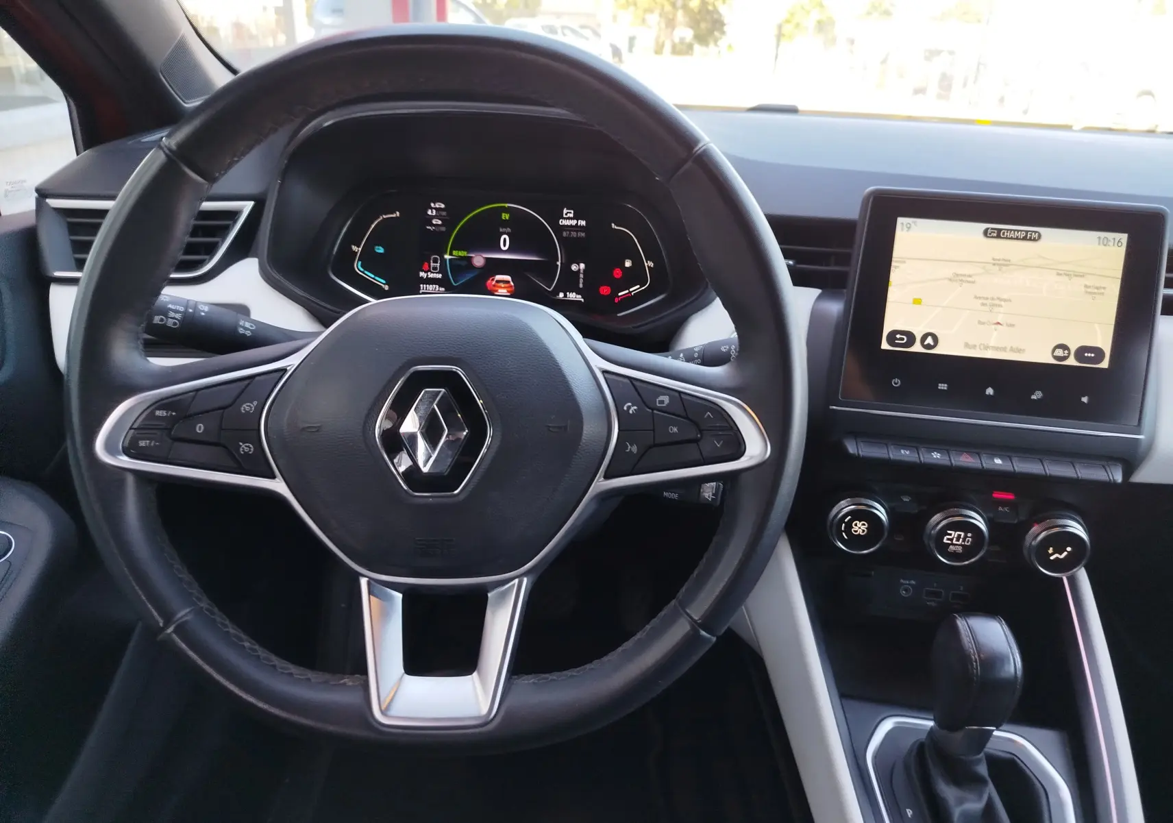 Vue intérieure centrée sur le volant noir de la Renault Clio hybride avec tableau de bord numérique et écran tactile.