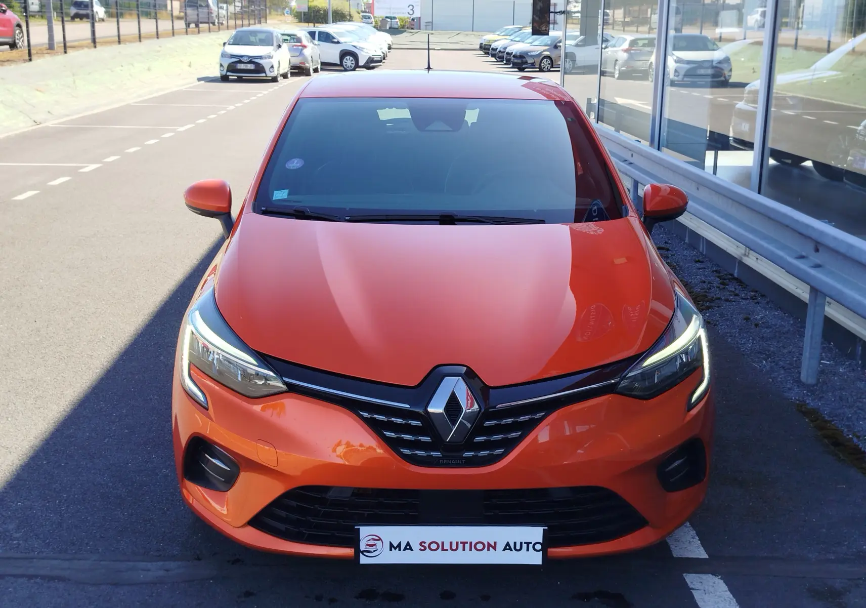 Vue avant d'une Renault Clio 1.6 E-Tech hybride 140ch Intens 2022 en orange Valencia avec phares LED allumés.