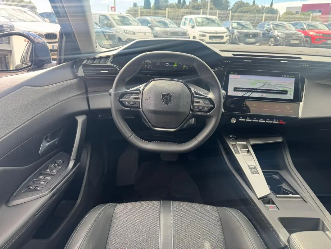 Vue intérieure avant du Peugeot 308 Hybrid gris, montrant le volant compact, le cockpit numérique et l'écran tactile central.