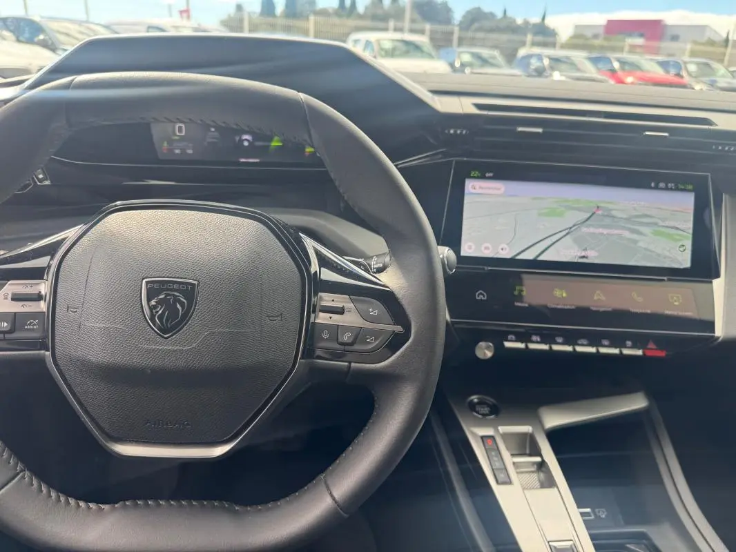 Vue intérieure centrée sur le volant Peugeot et le cockpit numérique avec écran tactile de navigation.