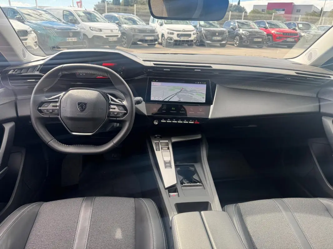 Vue intérieure avant du Peugeot 308 Hybrid gris, avec volant compact, écran tactile central et console moderne.