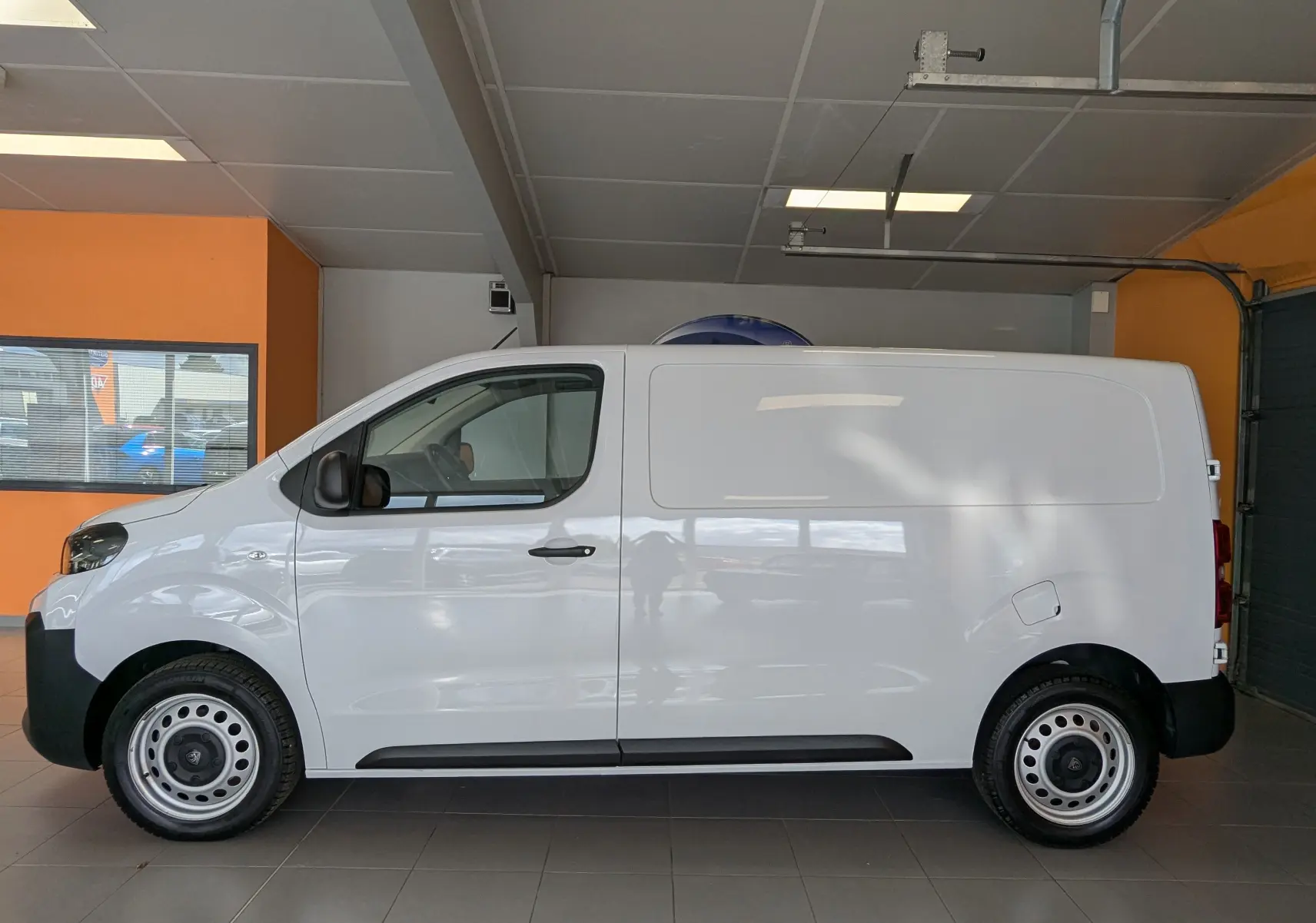 Vue latérale droite d'un Peugeot Expert Fourgon blanc 2024 avec jantes tôles 17 pouces en intérieur showroom.