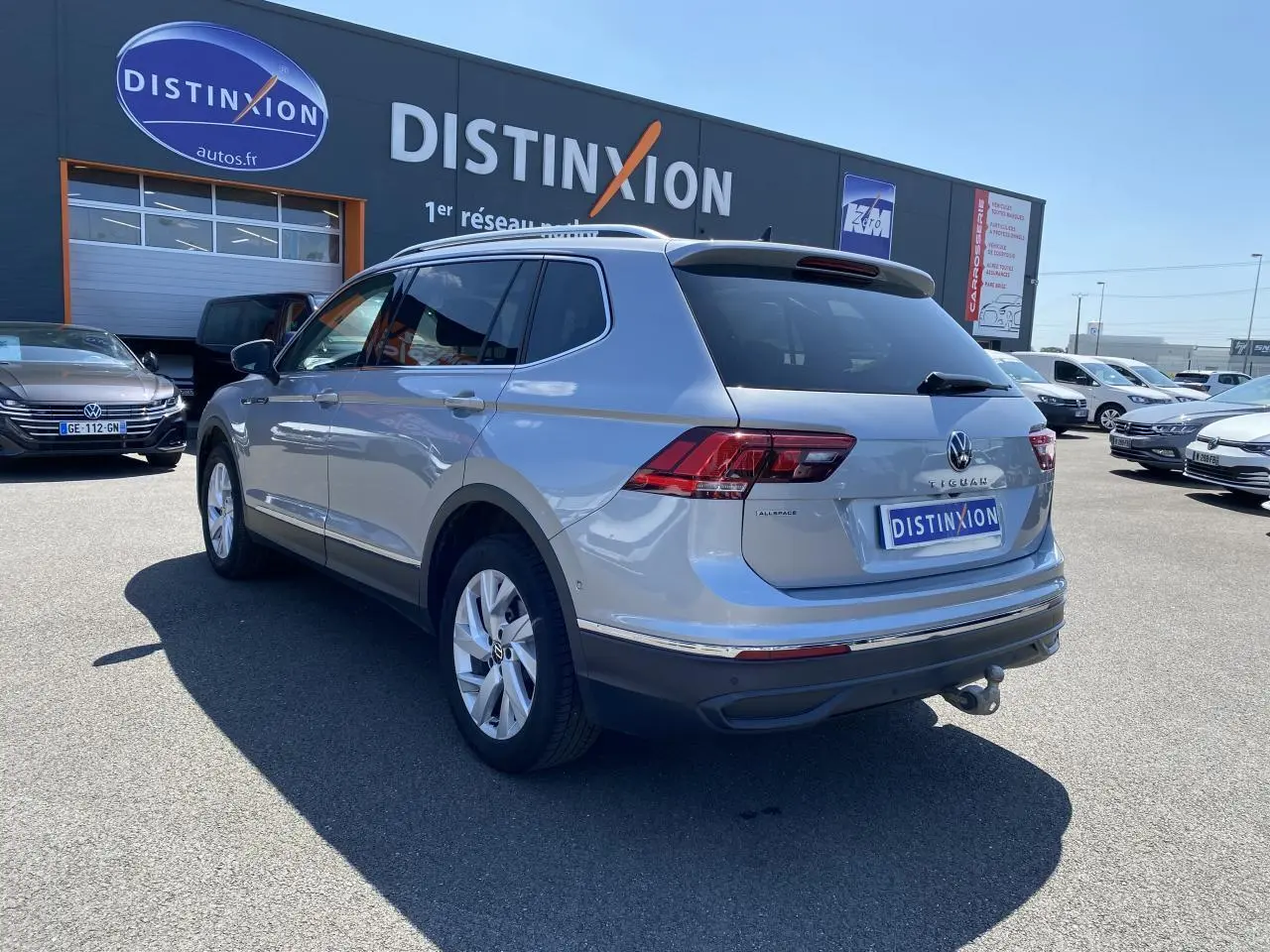 Volkswagen Tiguan Allspace gris argent vu en 3/4 arrière droit avec crochet d'attelage escamotable et vitres teintées.