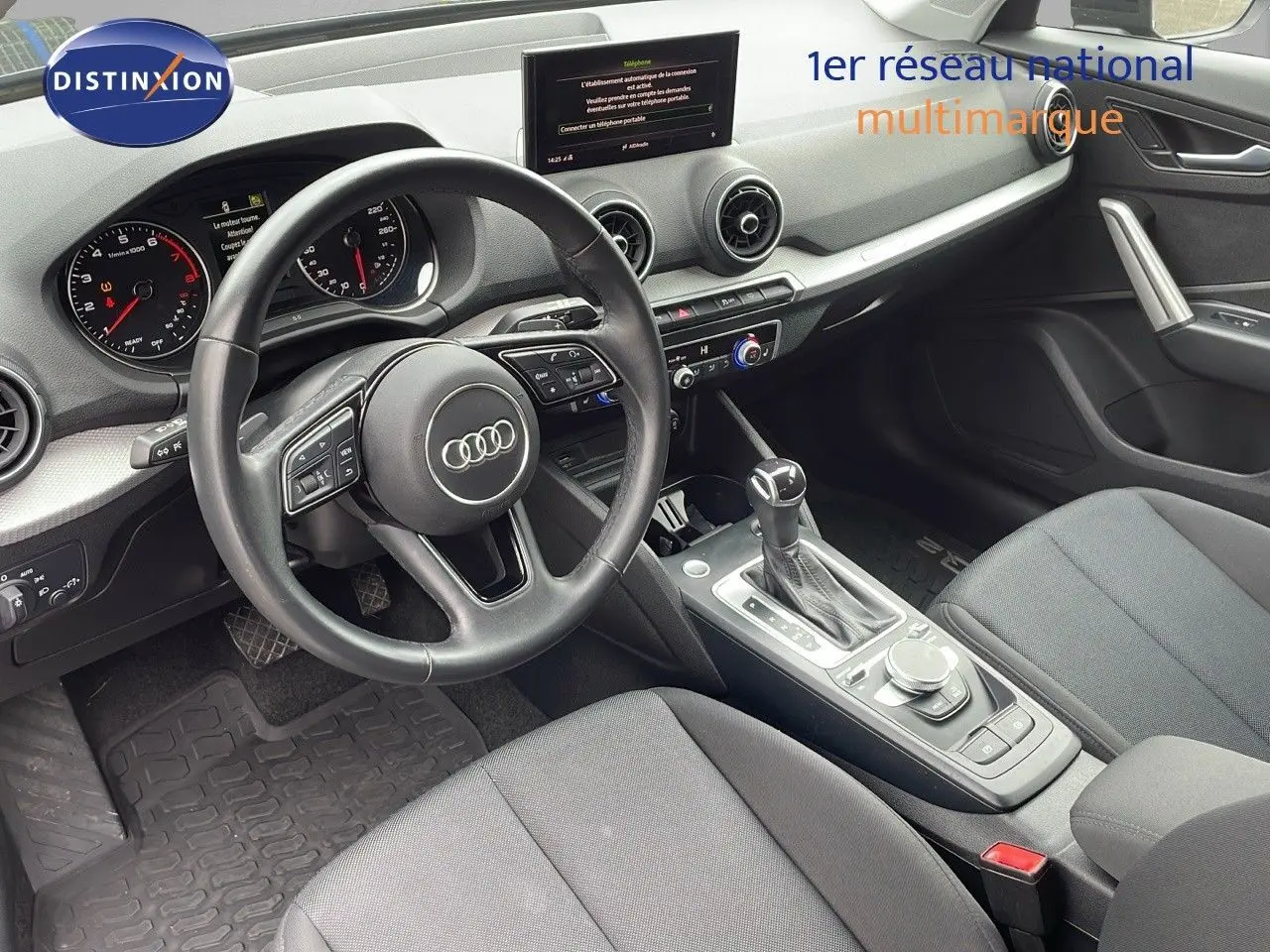 Vue intérieure de l'Audi Q2 35 TFSI 2023 montrant le volant, tableau de bord et console centrale avec boîte automatique.