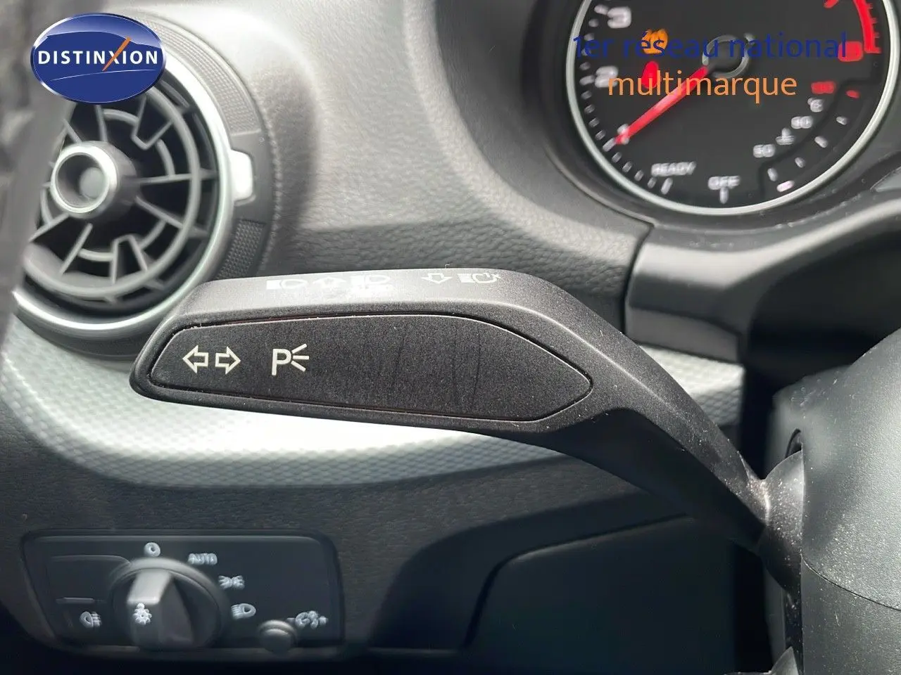 Gros plan sur la commande de clignotants à gauche du volant d'un Audi Q2 noir mito metal, tableau de bord en arrière-plan.