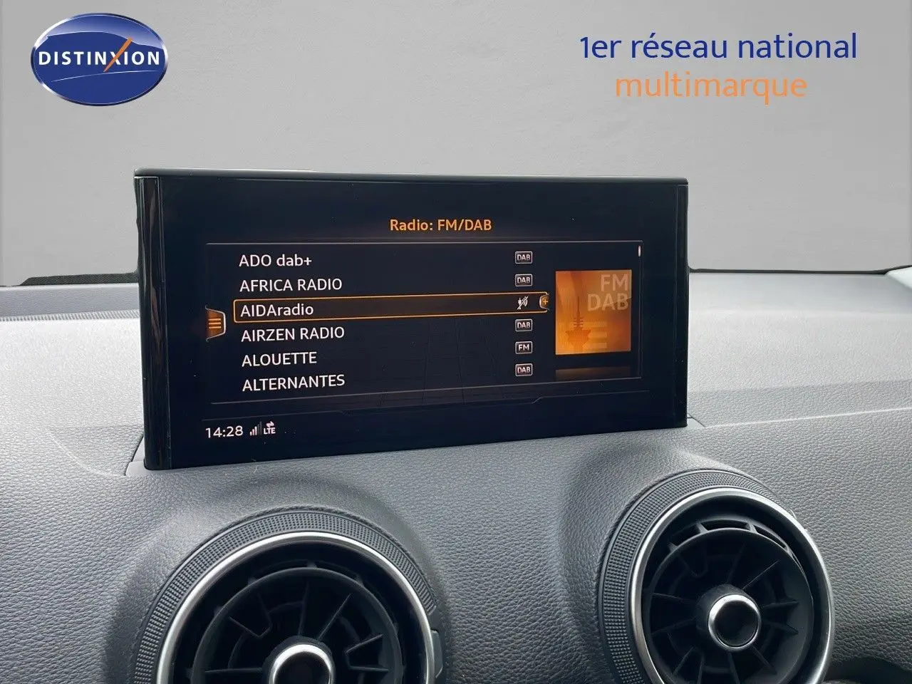 Écran multimédia affichant les radios FM/DAB sur le tableau de bord gris d'un Audi Q2 noir mito metal.