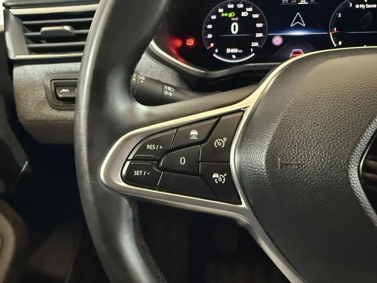 Gros plan sur le volant noir de la Renault Clio 2024 avec commandes de régulateur de vitesse et tableau de bord numérique.