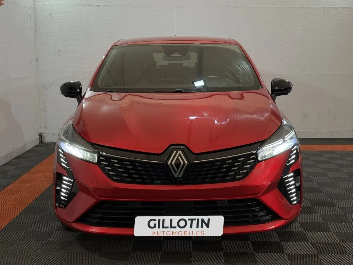 Vue frontale d'une Renault Clio Techno TCe 90 rouge avec feux LED allumés dans un garage.