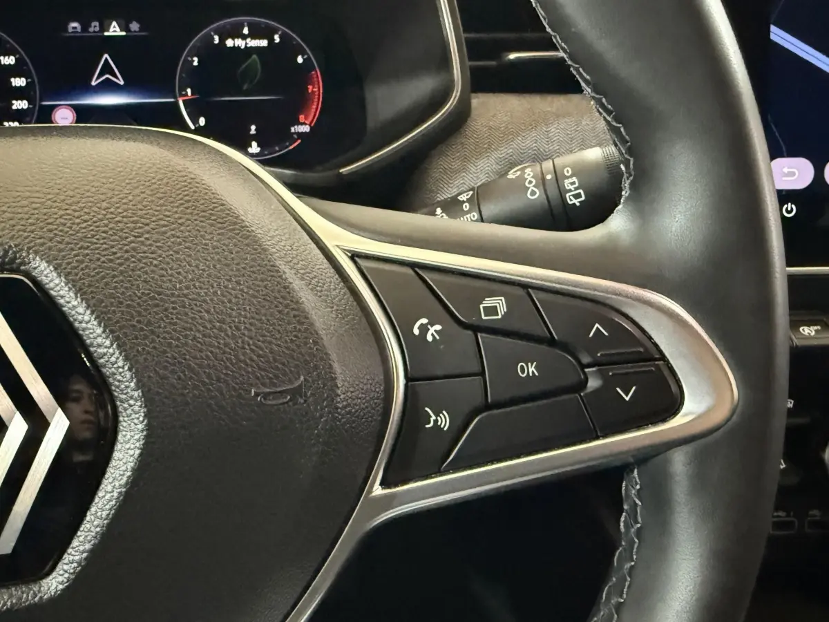 Gros plan sur le volant cuir noir de la Renault Clio 2024 avec commandes multifonctions côté droit et combiné numérique en arrière-plan.