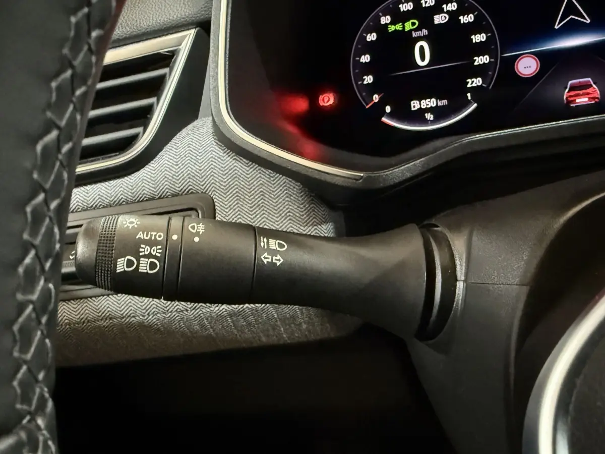 Gros plan sur la commande des phares à gauche du volant dans l’habitacle de la Renault Clio rouge 2024.