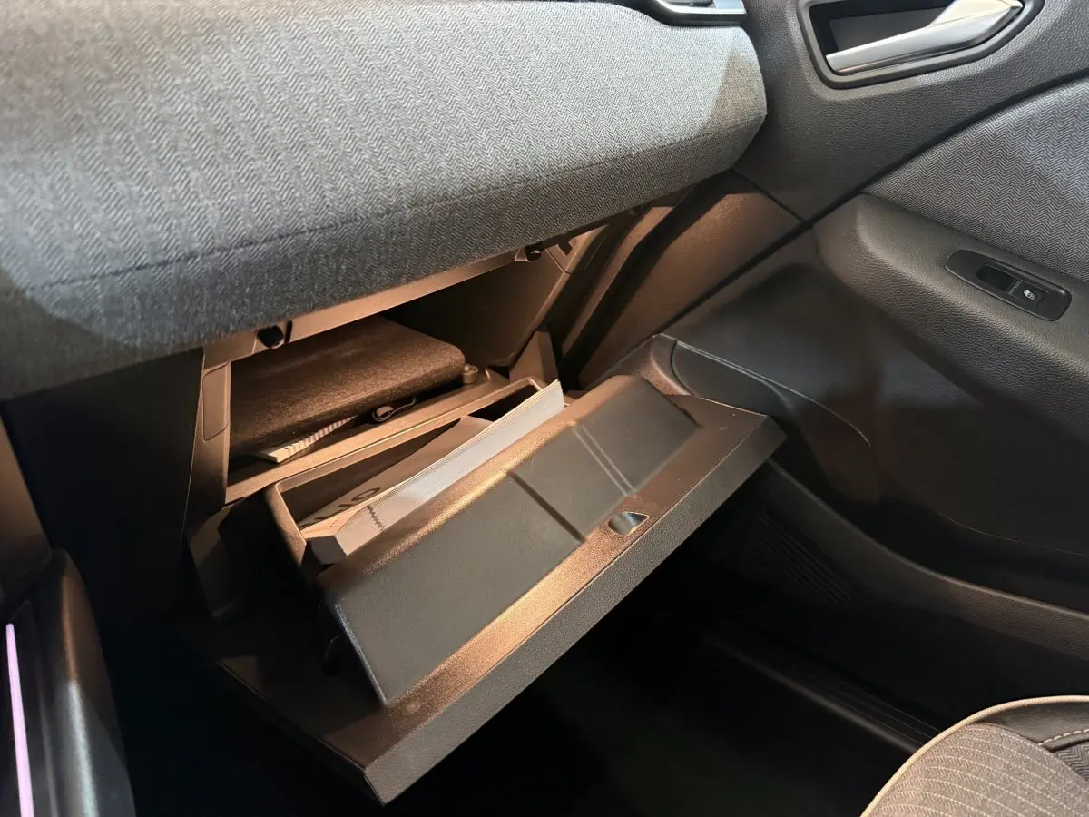 Gros plan de la boîte à gants ouverte côté passager dans l'habitacle sombre d'une Renault Clio rouge 2024.