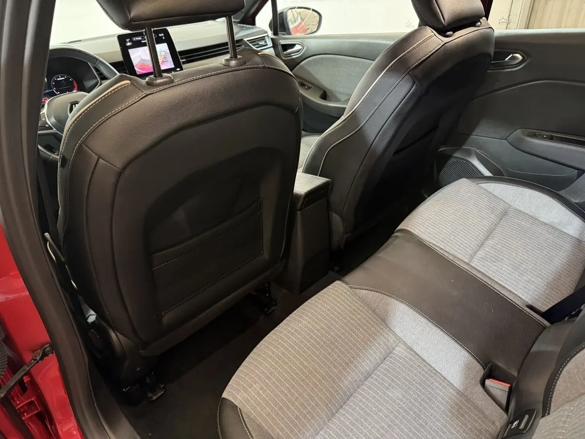 Vue intérieure arrière droite de la Renault Clio rouge 2024, sièges tissu gris et noir avec appuis-tête et écran tactile avant.