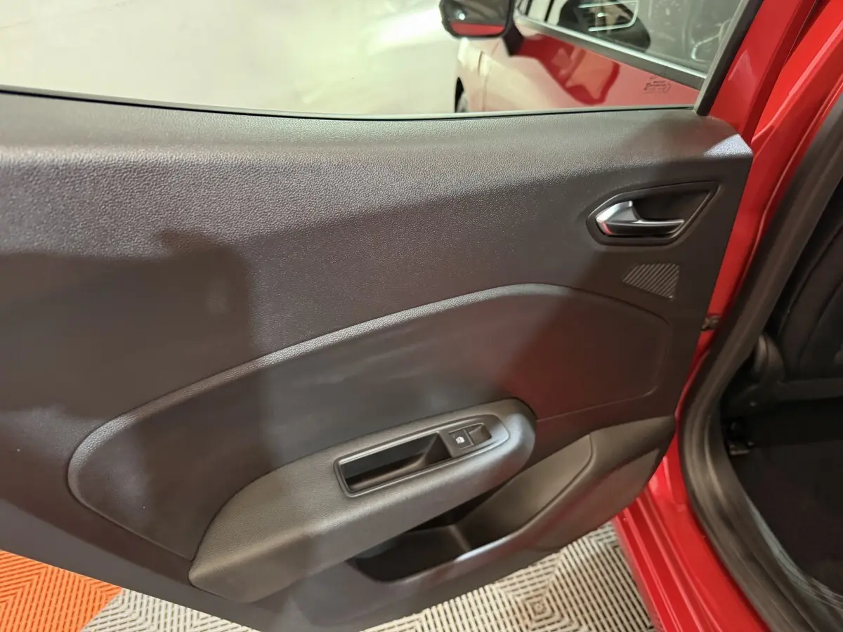 Vue intérieure sur la porte arrière gauche noire avec poignée et bouton de lève-vitre d’une Renault Clio rouge 2024.