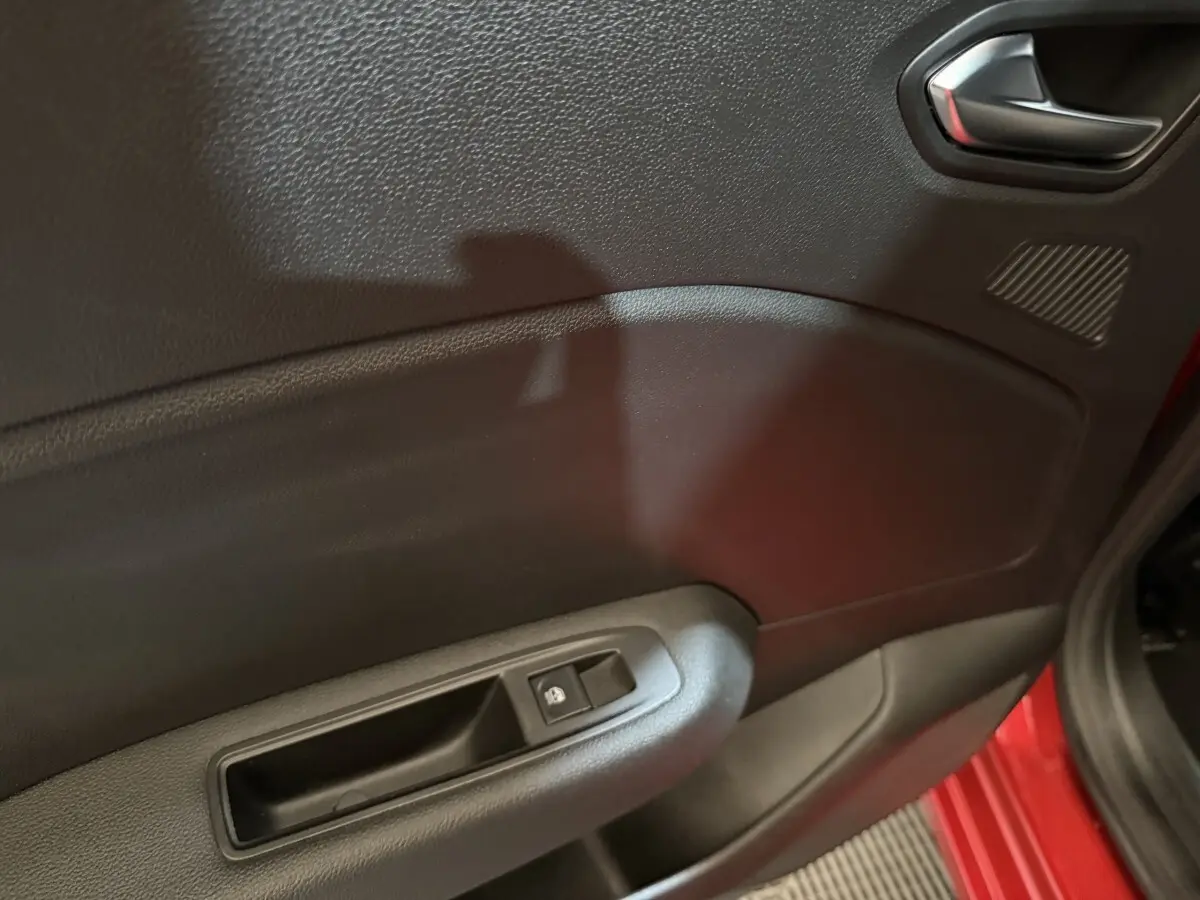 Vue rapprochée de la porte avant gauche rouge d’une Renault Clio 2024 avec commande de lève-vitre électrique.