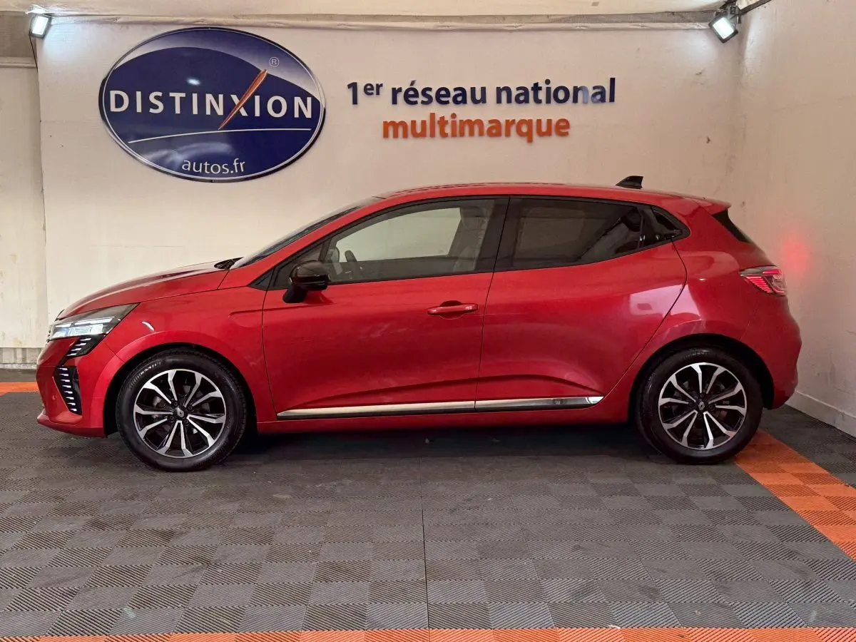 Profil côté gauche d'une Renault Clio Techno TCe 90 rouge 2024, avec jantes alliage et feux arrière LED allumés.