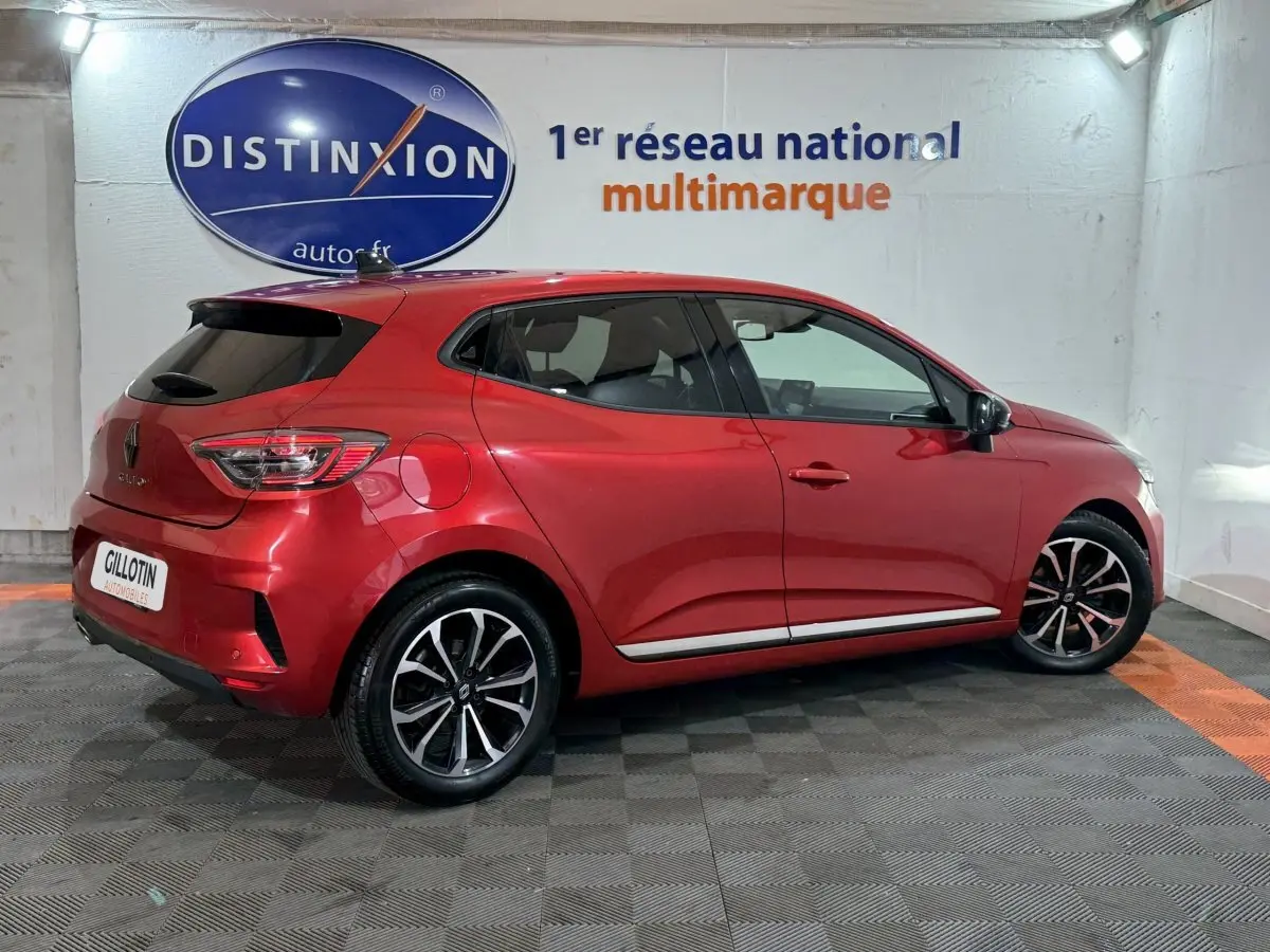 Vue 3/4 arrière droite d'une Renault Clio Techno TCe 90 rouge 2024 avec jantes alliage et feux LED.