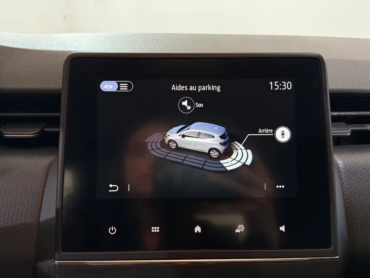 Écran tactile intérieur montrant l'aide au parking arrière d'une Renault Clio blanche, vue de dessus stylisée.