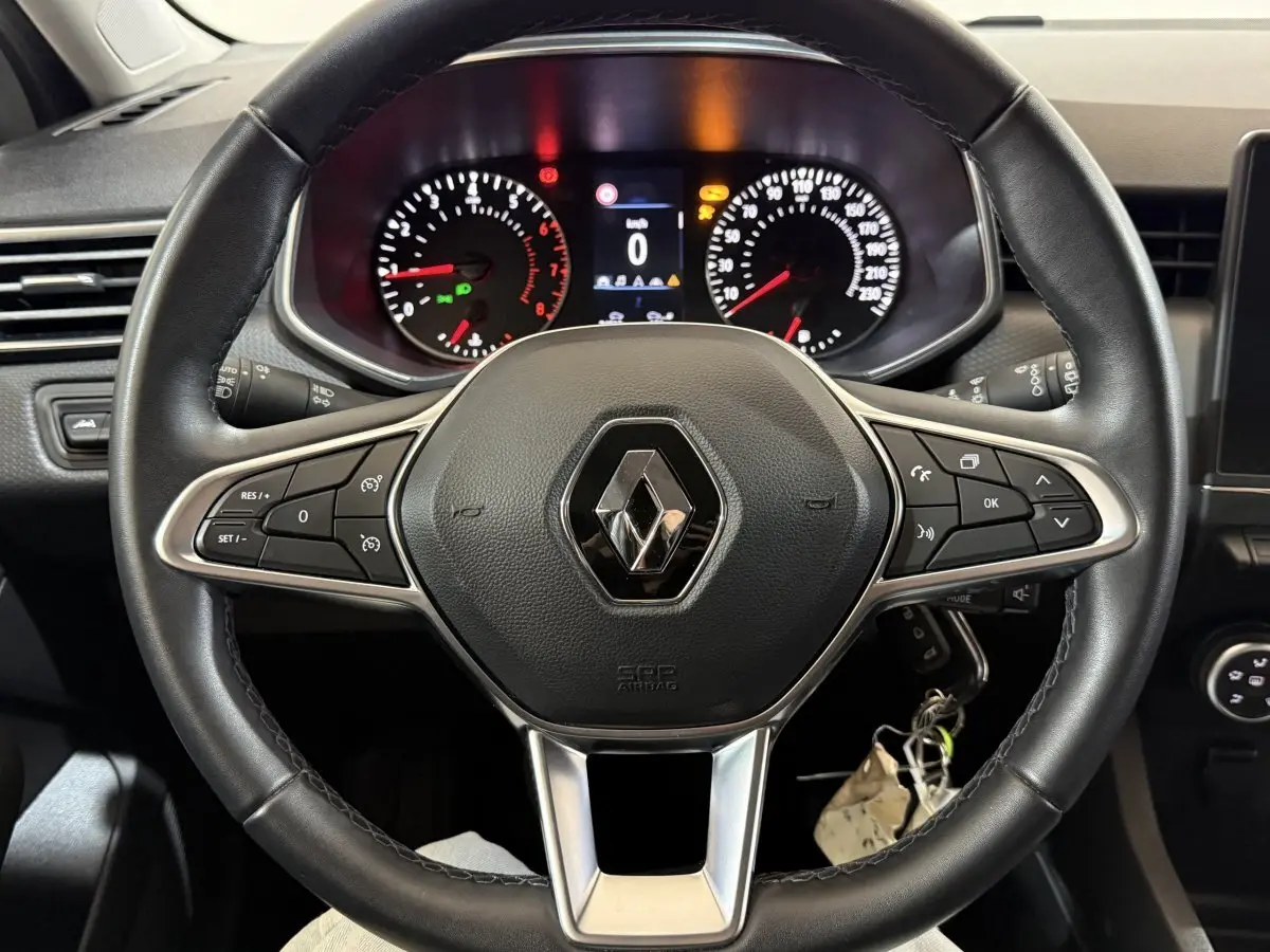 Vue rapprochée du volant cuir noir multifonctions d'une Renault Clio blanche avec tableau de bord et compteurs éclairés.